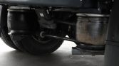 Underside of a heavy truck: rear wheel, axle, exhaust pipe, and a rusted cylindrical tank visible beneath the chassis.