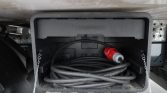 Coiled heavy-duty electrical cable stored in a trailer/vehicle power box with a red plug attached.