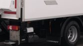 Rear lower side of a white cargo truck showing a large wheel, mudflap marked LAMBERET, and utility components near the bumper and taillight cluster.