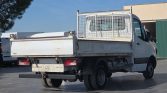 White flatbed truck with a metal cage on the back, parked in an outdoor lot under a clear blue sky