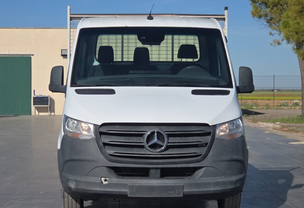 Front view of a white Mercedes-Benz cargo van parked outdoors, showing grille, headlights, and side mirrors at the front.