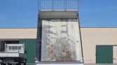 Industrial yard with a raised, rusty metal dump truck bed preparing to unload.