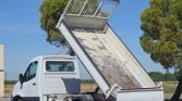 White cab truck with a raised rust-streaked dump bed, in an open lot under a clear blue sky, as if unloading material.