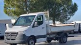 White Mercedes-Benz flatbed truck parked in a lot with a large tree behind it.