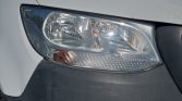 Close-up of a car headlight on a white vehicle, with an amber turn signal and gray bumper.
