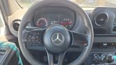 Close-up of a Mercedes steering wheel with mounted controls, the instrument cluster behind it, and a manual gear stick to the right.