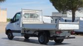 White flatbed utility truck with a metal mesh cargo cage behind the cab, parked in an industrial lot.