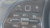 Close-up of a car steering wheel cruise control panel showing RES, SET+ and SET- with CNCL and LIM labels and a central square button while a textured roller sits in the middle.