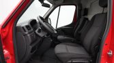 Interior view of a red van cabin: driver and passenger seats with dark upholstery and a steering wheel on the left side, dashboard, and floor mats visible.