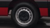 Close-up of a car wheel: black tire mounted on a silver steel rim with circular holes, next to a red vehicle body.