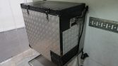 Industrial diamond-plate metal cabinet/cooler mounted in a corner, with a black top and an attached power cord hanging on the side.
