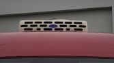 Pink truck cab with a beige roof-mounted Carrier refrigeration unit featuring black vent slots and a blue Carrier badge on top