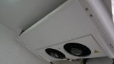 Ceiling-mounted air conditioning unit with two circular fans and a warning label on the side.