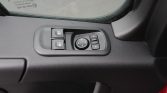 Driver-side door control panel with two window switches, a circular mirror adjustment dial, and a small joystick-style button nearby on a textured black door panel.