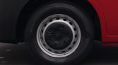 Close-up of a car wheel with a silver steel rim and black center cap under a red vehicle surface.