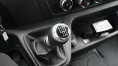 Manual gear shift knob with six gears (R, 1-6) and leather boot inside a car cabin, with climate control dials above and a small device on the center console.