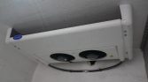 White Carrier outdoor air conditioner condenser with two fans mounted on a white wall or ceiling edge, with piping visible below.