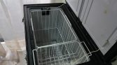 Open chest freezer with white wire baskets inside and a dusty frost on the bottom.