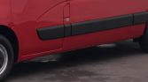 Close-up of the lower side of a red cargo van, showing black protective rocker panels and a small badge on the door.