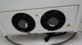 Outdoor HVAC condenser with two large circular fans mounted on a white wall, shows wiring and protective conduit nearby.