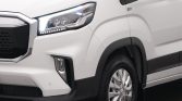 Close-up of a white van's front left corner, showing the headlight, bold grille, and front wheel with tire tread visible.