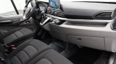 Interior of a vehicle showing the driver seat, steering wheel, center touchscreen, and front passenger area.