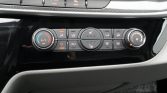 Car climate control panel with left temperature dial, central airflow and seat heater buttons, and right fan dial.