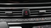 Car dashboard center with hazard and HOME button; row of control switches below and climate dials nearby.
