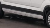 Side view of a white van with black lower trim and visible wheel, parked on a paved surface.