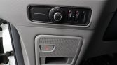 Car interior: driver-side panel with circular headlight control dial and small adjacent switches, and a gray SOS button on a perforated speaker panel below.