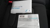 Two sealed booklets on a car back seat: 'MAXUS eDELIVER 9' warranty handbook and related documents.