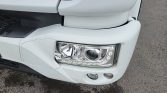 Close-up of a white truck's front-left corner showing the headlight and bumper details.
