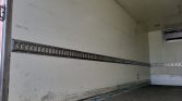 Empty truck trailer interior with a long row of metal E-track tie-down rails along the wall and a scuffed lower edge of the floor.