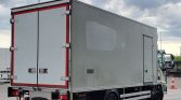 Large grey box truck with a cargo trailer, viewed from the rear-left, parked in a lot with red detailing around the doors.