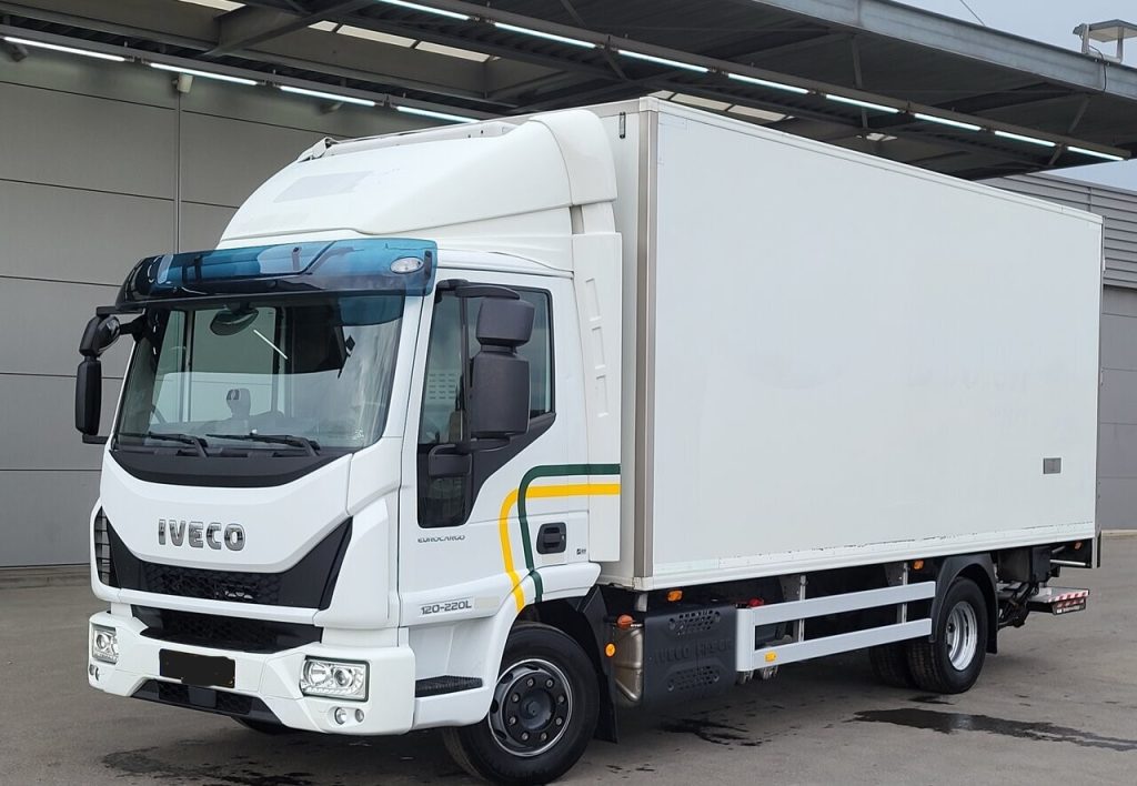 White Iveco box truck parked at a loading dock with a large rectangular cargo box behind the cab.