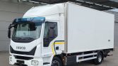 White Iveco box truck parked at a loading dock with a large rectangular cargo box behind the cab.
