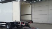 White delivery truck with rear doors open and a lowered metal loading ramp at a loading dock.