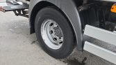 Close-up of a heavy-duty truck wheel: silver rim, black Continental tire, mudguard, and undercarriage on a wet concrete surface.