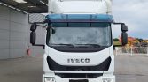 Front view of a white Iveco truck facing the camera in an industrial yard, with a large black grille and headlights visible
