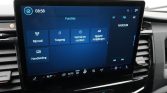 In-car infotainment screen showing 'Functies' tiles: Rijmodi, Toegang, Vertrek en comfort, Oplaad-instellingen, Handleiding, with climate controls below