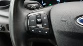 Close-up of a car steering wheel with cruise control buttons (CAN, RES, SET+, SET-, LIM) on the left, and a faint dashboard display in the background.