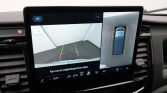 In-dash display showing rear camera view with green/yellow/red guiding lines for parking, plus a separate top-down bird's-eye view of the car in a parking space on the right.