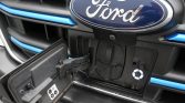 Front of a Ford EV with the charging port cover open, exposing the circular charging inlet and blue trim accents.
