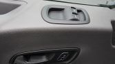 Close-up of a car door interior showing window control switches on a textured gray panel with a door handle nearby and a lock button below