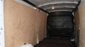 Interior of a white cargo van with plywood side panels and a black rear door at the far end.