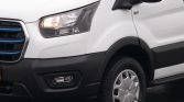 White commercial van front-left view, showing headlight, grille with blue accents, and front tire/wheel.