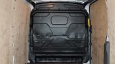 Empty white cargo van interior with wooden side panels and a black bulkhead at the back, viewed from inside the cargo area.