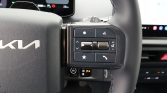 Close-up of a car steering wheel with multifunction controls: volume roller, arrow pad, phone, and star buttons, plus a gear selector below.