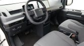 Driver's cockpit with steering wheel, digital gauges, and a large central touchscreen in a gray-car interior.