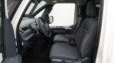 Front cabin of a modern van: driver and passenger seats, steering wheel, and dashboard visible with a light interior.